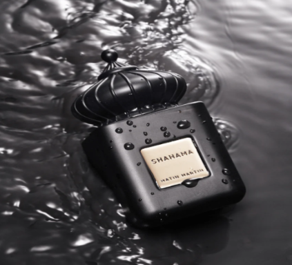 A black bottle of Shahama EDP 100ml by Matin Martin with a crown-like cap, set against a blurred background with water droplets.
